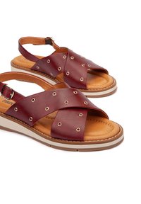 Sandalias de cuero burdeos con diseño de tiras cruzadas, acentos metálicos redondos y una plantilla acolchada en tono marrón; con una correa tipo slingback y suela plana.