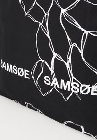 Borsa tote nera con motivo a catena bianco, caratterizzata da un audace marchio "SAMSOE" in bianco. Realizzata in resistente materiale di tela.