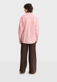 Pink striped long-sleeve shirt with a back pleat detail, worn with brown wide-leg corduroy pants. Textured fabric and relaxed fit.