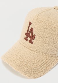 Gorro de lã castanho claro com superfície texturizada, apresentando um logótipo "LA" bordado em castanho na frente, e uma aba curva.