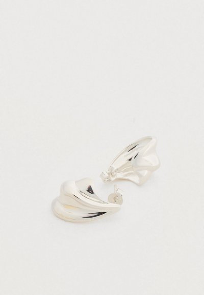 Ασημένια σκουλαρίκια με ρέον, καμπυλωτό σχέδιο. Λείο μεταλλικό υφή, με γυαλιστερό φινίρισμα και ασφαλές κούμπωμα πίσω με καρφί.