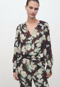 Blusa floral fluida en marrón oscuro, con flores en menta y crema, con escote en forma de V, hombros fruncidos y mangas largas.