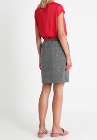 Blusa rossa a maniche corte abbinata a una gonna a tubino grigia con texture, dotata di uno spacco sul retro e semplici scarpe slittanti rosa.