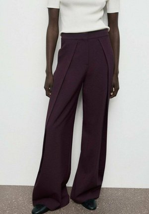 Pantalones de pierna ancha en tejido burdeos oscuro, con pliegues, cintura alta y una textura suave. Combinados con una blusa ajustada blanca y zapatos negros.