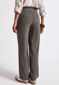 Byxor med elastisk midja och lös passform i en dämpad olivgrön färg. Har två bakfickor och en mjuk textur. Matcher med lätta sneakers.