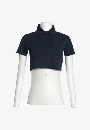 Camiseta polo negra corta y recortada con cuello y tres botones, mostrada en torso de maniquí blanco con brazos.