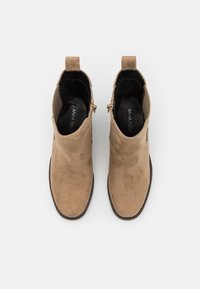 Light beige suede ankle boots with a smooth texture, zip closure on the side, and a short pull tab at the back.
