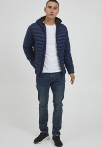 Námornícka prešívaná bunda s predným zipsom a kapucňou, s horizontálnym prešívaním a hladkým povrchom, skombinovaná s pohodlnými džínsami.