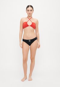 Haut de bikini rouge avec un design de bretelles entrecroisées et un centre découpé, associé à un bas de bikini noir taille haute avec un accent de logo.