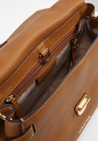 Sac à main en cuir brun à texture granuleuse avec une forme structurée, doté de quincaillerie dorée, d'une poche zippée et d'un intérieur en tissu.