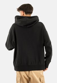 Felpa nera con un ampio cappuccio profondo, maniche lunghe e vestibilità rilassata. Il materiale sembra morbido e testurizzato, con un design di colore uniforme.