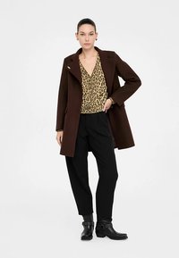 Brązowy wełniany płaszcz z szerokim kołnierzem, zestawiony z bluzką w panterkę i czarnymi spodniami. Czarne botki na kostkę z ozdobną klamrą.