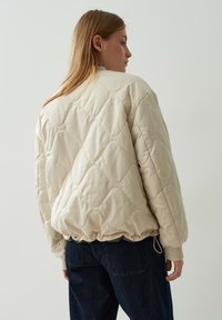Gepolsterte Bomberjacke in hellbeige mit gestepptem Muster, gerippten Bündchen und einem verstellbaren Kordelzugsaum.