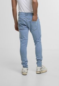 Vaaleansiniset slim fit -farkut, joissa on kulunut pinta, tavalliset taskut ja vyötärönauha. Yhdistettynä valkoisiin lenkkareihin.