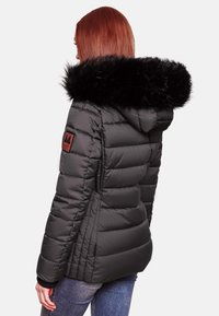 Black padded jacket with a detachable black faux fur hood, ribbed cuffs, and a logo patch on the left sleeve, featuring vertical seams.