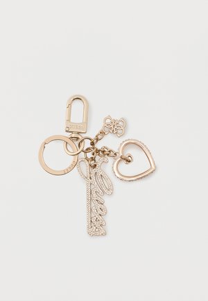 Llavero en tono dorado con clip mosquetón, aro circular, charm con la palabra "Guess" en cursiva y cristales, charm de corazón entrelazado y pequeño charm con el logotipo de la marca.