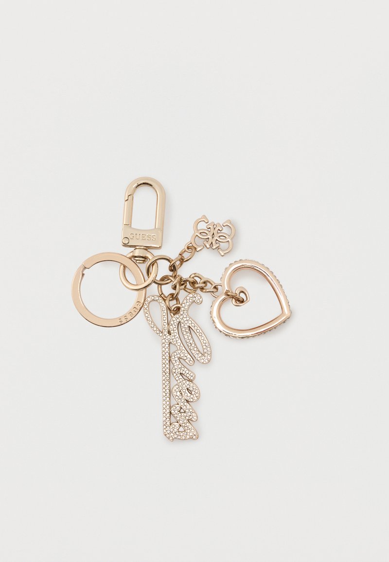 Μπρελόκ σε χρυσό τόνο με κλιπ καραμπινέρ, κυκλική κρίκο, γούρι με την επιγραφή "Guess" και κρύσταλλα, διαπλεκόμενη καρδιά και μικρό γούρι με το λογότυπο της μάρκας.