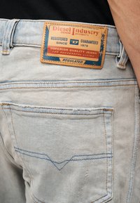 Κοντινή λήψη πίσω τσέπης ανοιχτό μπλε τζιν με φθαρμένη δερμάτινη ετικέτα Diesel Industry ραμμένη πάνω από την τσέπη.