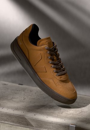 Brune ruskinds sneakers med perforeret tåhætter, brune snørebånd og en kontrasterende mørkegrå sål. Minimalistisk design med logo accenter.