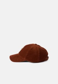 Braune Corduroy-Baseballmütze mit gebogenem Schild, strukturiertem Stoff und verstellbarem Riemen hinten. Auf der Seite befindet sich ein Logo-Patch.