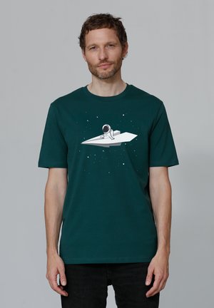 Dark green cotton t-shirt featuring a white astronaut graphic on a paper airplane, with scattered star motifs on the fabric.