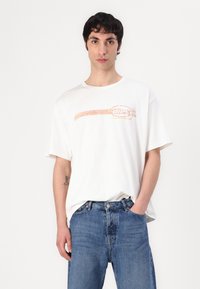 White cotton t-shirt featuring a colorful "Diesel" logo print. Relaxed fit with short sleeves, paired with light blue denim jeans.
