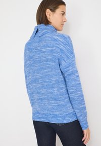 Pull bleu tricoté avec un col côtelé, variation de texture, et coupe légèrement ample, assorti à un jean foncé pour créer un contraste.