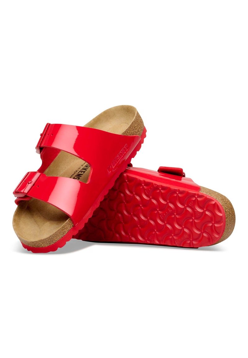 Rote Sandalen mit zwei Riemen, verstellbaren Schnallen, Korkfußbett und strukturierten roten Gummisohlen, gezeigt mit einem Sandalenpaar, bei dem ein Sandale auf der anderen ruht.