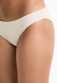 Beige katoenen bikinislipje met een gladde textuur, voorzien van een taille die laag zit en minimale stiksel details. Zacht, aansluitend ontwerp.