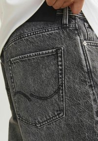 Lähenemisest isik, kes kannab kulunud musti teksaseid, millel on eristuv tagakoti õmblus ja valge särk sisse pandud.