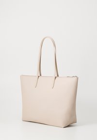 Sac fourre-tout beige en matériau texturé avec deux longues poignées, de forme rectangulaire et une fermeture éclair sur le dessus. Design lisse et minimal.