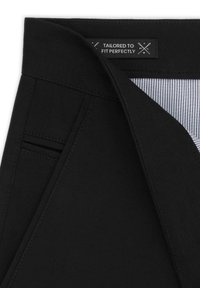 Czarne spodnie dopasowane, wykonane z gładkiego materiału, z etykietą na pasku brzmiącą "DOPASOWANE, ABY IDEALNIE PASOWAŁY" oraz subtelnymi detalami kieszeni.