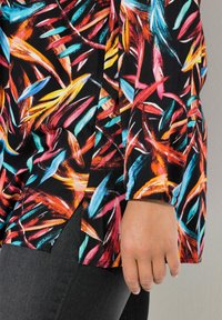 Tessuto colorato con un motivo floreale nei toni di rosso, arancione, blu e nero. Presenta una vestibilità ampia con una leggera apertura all'orlo.