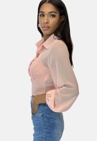 Cropped blouse rosa chiaro con colletto, maniche a palloncino e vita elasticizzata, abbinata a jeans in denim blu a vita alta.