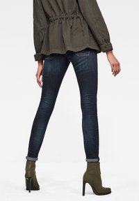 Jeans skinny de color azul oscuro con una textura desvanecida, combinados con botas de tobillo verde oliva con tacones en forma de cono y una blusa de canalé.