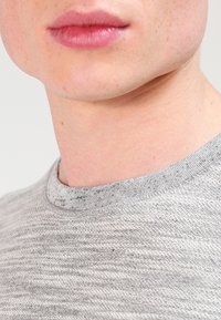 Suéter gris de punto texturizado con cuello redondo, que presenta variaciones sutiles en el hilo y un acabado suave.