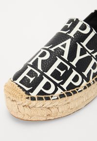 Espadrilla nera con scritte bianche. Presenta una parte superiore in pelle testurizzata, punta tonda e suola in juta intrecciata di colore naturale.