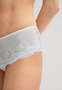Witte kanten boyshorts met een bloemenpatroon en golvende randen, van een zachte, doorschijnende textuur en met een comfortabele tailleband.