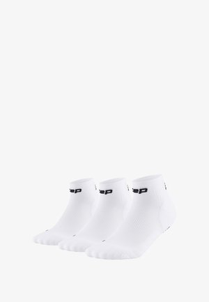 Trois paires de chaussettes de cheville blanches avec un design côtelé et un logo noir sur les poignets. Texture lisse et orteils arrondis.