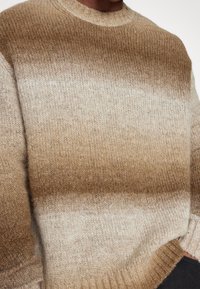 Beżowo-brązowy sweter z dzianiny w gradientowy wzór, z prążkowanym dekoltem i mankietami, charakteryzujący się miękką teksturą i subtelnymi odcieniami kolorów.