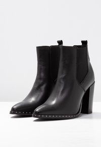 Stivali ankle in pelle nera con punta appuntita e tacco largo, dotati di pannelli laterali elasticizzati e dettagli in metallo argento lungo la suola.