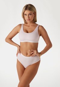 Lichtroze geribbelde bralette en hoog-waisted bikini set. Heeft een scoop halslijn, geschulpte randen en een zachte textuur. Minimalistisch ontwerp.