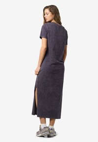 Tmavo fialové, šaty po členky s krátkymi rukávmi, bočným rozparkom a mäkkou textúrou látky. Neformálny dizajn, nosené s šedými teniskami.