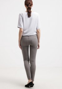 Grå slim-fit byxor med fem fickor, matchade med en ljusgrå kortärmad topp. Modellen ses från baksidan. Svarta skor fulländar outfiten.