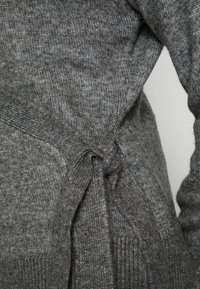 Grå stickad tröja med en texturerad väv, med knytmidja och ribbade ärmslut, vilket ger en distinkt känsla av värme och komfort.