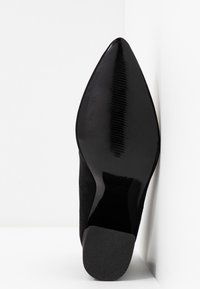 Black pointed-toe shoe with a smooth patent leather finish. Features a textured sole and a soft suede upper, creating a contrasting appearance.