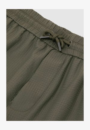 Olívazöld, texturált szövetnadrág rugalmas derékpánttal és fém végződésű, megkötött húzózsinórral.