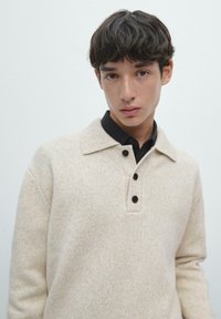 Sweter dziany w jasnobeżowym kolorze z fakturowanym wykończeniem, z kołnierzykiem i trzema czarnymi guzikami na rozporku.