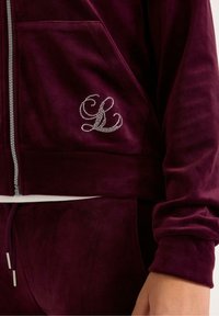 Bordeaux velours zip-up jack met een decoratieve kristallen monogram op de linkerpocket, geborstelde textuur en geribde boorden.