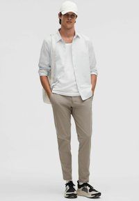 Jasnoszara koszula zapinana na guziki noszona na białym topie, beżowe spodnie, czarno-białe trampki i biała czapka. Codzienny strój o minimalistycznym designie.